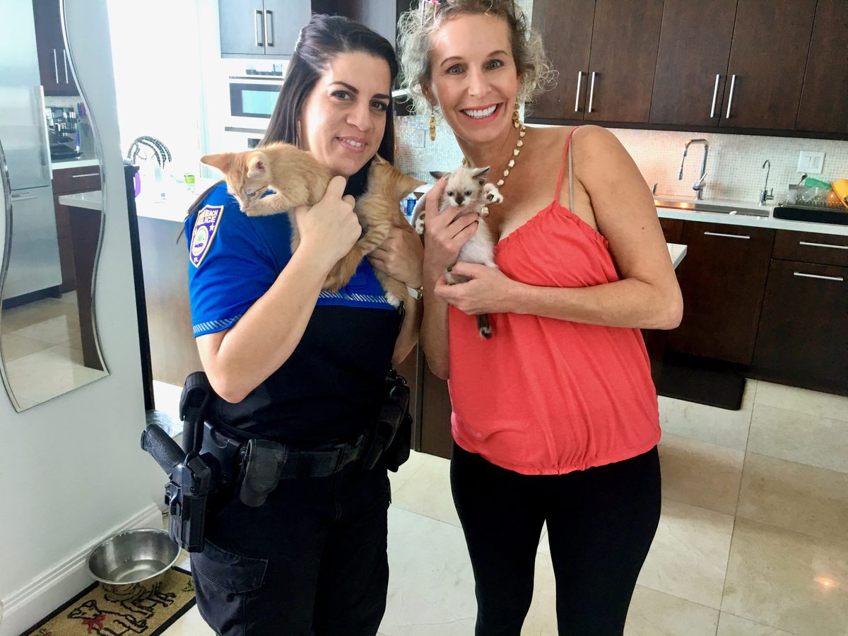 Two women holding three rescued kittens in a kitchen, one wearing a police uniform